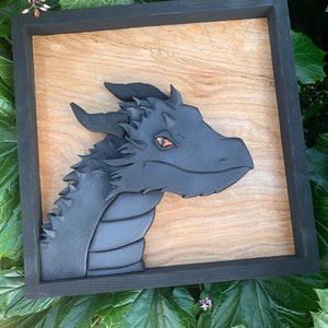 May include: A black dragon head sculpture in a wooden frame. The dragon has a textured, scaly body and orange eyes.