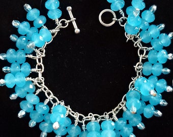 May include: A silver chain bracelet with a toggle clasp features a cluster of light blue faceted beads. The beads are arranged in a cascading design.