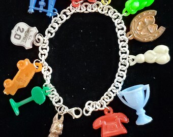May include: A silver charm bracelet with a variety of colorful plastic charms, including a red airplane, a blue pair of binoculars, a green shamrock, a yellow rope, a white rabbit, a blue trophy, a red phone, an orange car, a green stop sign, and a brown horseshoe.