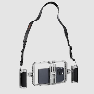 May include: Silver phone cage with a black phone inside, featuring a black leather strap and two black and silver handles. The strap has the word "COMO" printed in orange. The cage is designed to hold a phone.