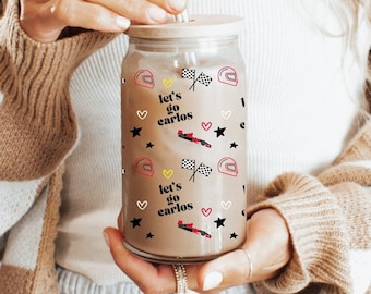 May include: A clear glass reusable water bottle with a white lid and a straw. The bottle has a pattern of black stars, red hearts, and the text "Let's go Carlos" repeated multiple times.
