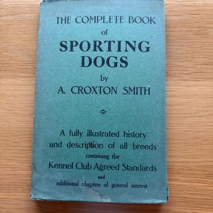 Puede incluir: Un libro vintage de color verde azulado titulado "THE COMPLETE BOOK of SPORTING DOGS" de A. Croxton Smith. El libro describe la historia y las razas de perros deportivos, incluidas las normas del Kennel Club.
