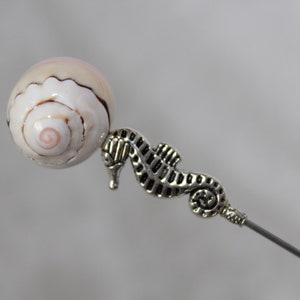 May include: A silver seahorse charm attached to a white seashell bead. The bead has a pink and brown swirl pattern.
