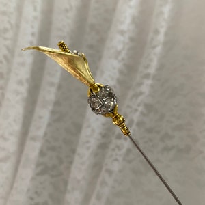 Puede incluir: Alfiler de sombrero dorado con dise&ntilde;o de cala. El lirio tiene un p&eacute;talo texturizado y un peque&ntilde;o acento de cristal brillante. El alfiler presenta una bola redonda con incrustaciones de cristal y una aguja larga plateada.
