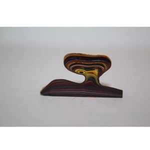May include: A unique, abstract sculpture with a layered design. The sculpture features a base and a curved top, with visible layers of various colors including brown, yellow, and red. The artwork is set against a plain white background.