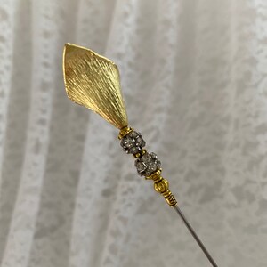 以下が含まれることがあります： 葉っぱの形をした装飾的なトップと、2列のクリアなラインストーンが付いた、ゴールドトーンのヘアピンです。