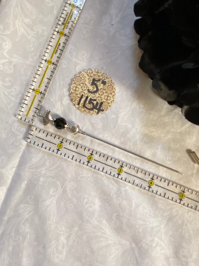 Puede incluir: Un alfiler de plata y negro con cuentas y un dise&ntilde;o decorativo de espiral. El alfiler mide aproximadamente 5 pulgadas de largo y se muestra sobre una superficie blanca con una regla.