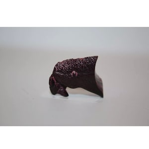 May include: A small, dark purple, irregularly shaped piece of pottery with a textured surface.