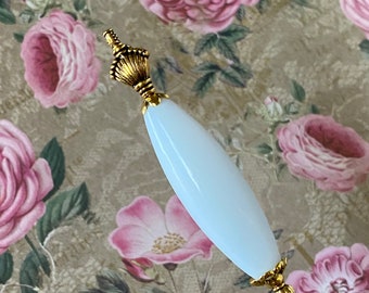 May include: A white glass pin with a gold metal top. The pin is on a floral background.