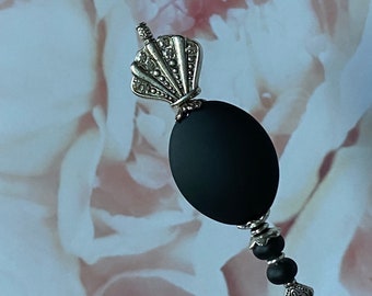May include: A decorative black and silver pin with a matte black oval bead. The pin features a silver seashell-shaped top and a decorative silver base with black beads. The pin is designed for decorative purposes.