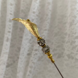 以下が含まれることがあります： 1つの花と2つの丸いクリアなラインストーンのアクセントが付いた、ゴールドトーンの金属製の花のピン