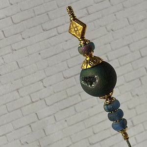 May include: A gold and blue beaded pin with a decorative flower design at the top. The pin is made of metal and glass beads.
