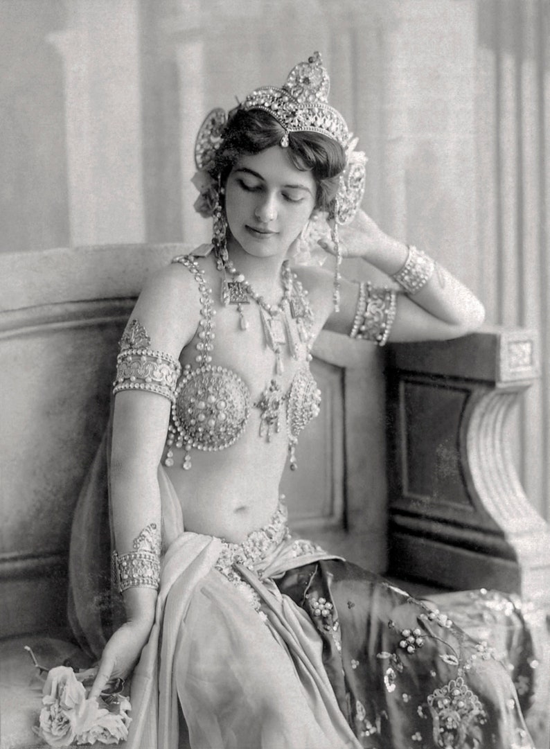 K&ouml;nnte beinhalten: Schwarz-Wei&szlig;-Fotografie einer Frau mit aufwendigem Schmuck, darunter ein Diadem, Armb&auml;nder und ein geschm&uuml;cktes Oberteil. Sie sitzt, h&auml;lt eine Blume und tr&auml;gt einen dekorativen Rock. Vintage-Stil.