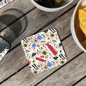 May include: A square coaster with a white background and a colourful pattern of various objects, including red shoes, a red dress, a yellow toaster, and a blue book.