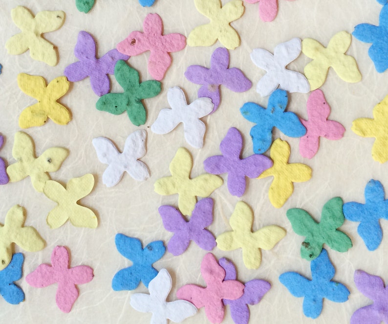 Puede incluir: Surtido de mariposas de papel de colores en varios tonos de azul, verde, amarillo, rosa y morado. Las mariposas est&aacute;n esparcidas sobre un fondo beige claro.