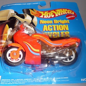 May include: A red and silver Hot Wheels Neon Bright Action Cycles motorcycle toy with blue and yellow stripes. The packaging is blue and features the Hot Wheels logo and the words "Neon Bright Action Cycles". The package also includes the words "Not for use with Hot Wheels sets" and "No. 2455".