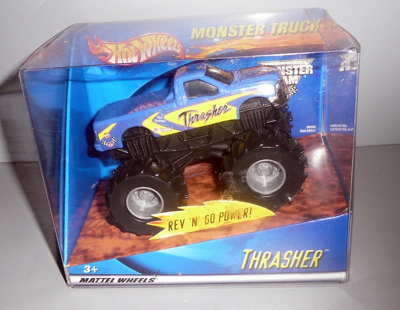 Może przedstawiać: Niebiesko-ż&oacute;łty samoch&oacute;d ciężarowy Hot Wheels Monster Jam Thrasher z dużymi kołami. Ciężar&oacute;wka znajduje się w przezroczystym plastikowym pudełku z niebiesko-ż&oacute;łtym tłem. Na pudełku widnieją napisy "Monster Truck" i "Thrasher".