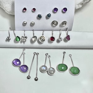 May include: Assortment of silver earrings with various gemstones, including amethyst, ruby, green, and moonstone. Some earrings feature a simple design, while others have intricate details like a flower or a butterfly.
