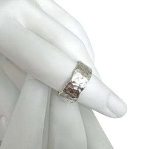 May include: A silver ring with a hammered texture. The ring is wide and has a textured surface. The ring is on a white background.
