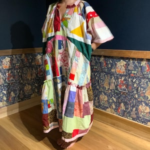 May include: A long, colourful patchwork dress with a V-neck and short sleeves. The dress is made of various fabrics in different colours and patterns, including floral, geometric, and plaid.