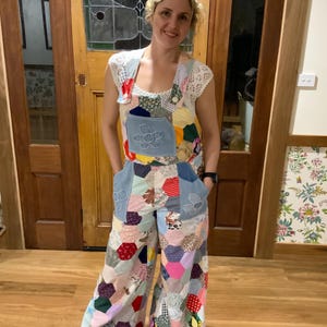 May include: A colourful patchwork jumpsuit with a bib top and wide legs. The jumpsuit is made from various fabric pieces in a geometric pattern. Denim pockets with flower appliqués are visible. A white lace top completes the outfit.