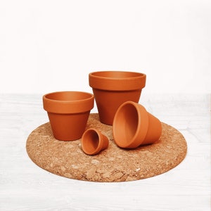 May include: Four terracotta pots of varying sizes, arranged on a cork trivet. The pots are all a similar shade of brown.