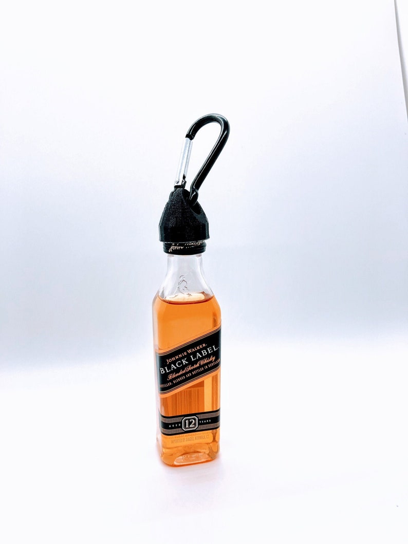 May include: A miniature bottle of Johnnie Walker Black Label Blended Scotch Whisky with a black carabiner attached to the top. The bottle is clear glass and the label is black with gold lettering. The bottle is 12 years old.