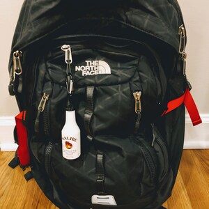 May include: A black North Face Borealis II backpack with a red and black zipper pull. A small clear bottle with a red and white label that says "Malibu" is attached to the zipper pull.