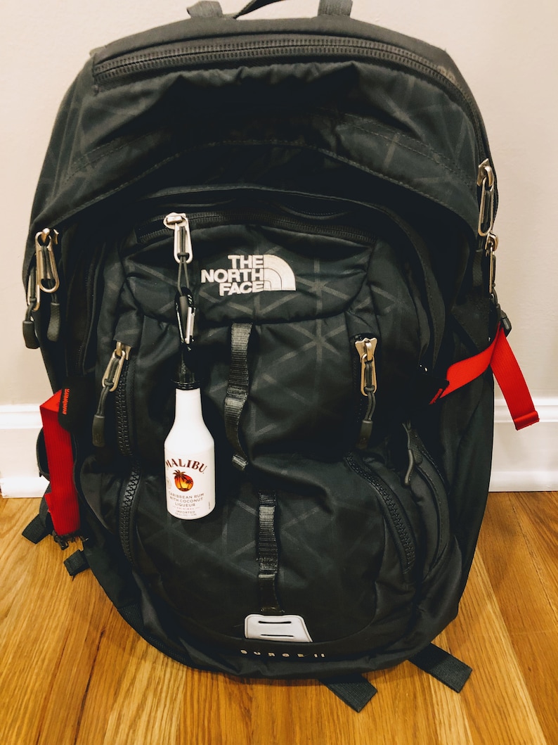 May include: A black North Face Borealis II backpack with a red and black zipper pull. A small clear bottle with a red and white label that says "Malibu" is attached to the zipper pull.