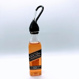 May include: A miniature bottle of Johnnie Walker Black Label Blended Scotch Whisky with a black carabiner attached to the top. The bottle is clear glass and the label is black with gold lettering. The label reads "Johnnie Walker Black Label Blended Scotch Whisky" and "12 Years Old".