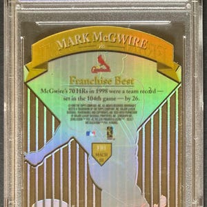 Puede incluir: Una tarjeta de b&eacute;isbol de Mark McGwire en un estuche protector. La tarjeta presenta una imagen hologr&aacute;fica de McGwire. El texto indica sus 70 jonrones en 1998. La tarjeta est&aacute; calificada y autenticada por Professional Sports Authenticator.