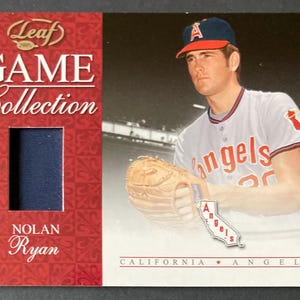 May include: A baseball card from the Leaf Game Collection featuring Nolan Ryan. The card has a photo of Ryan in his California Angels uniform, holding a baseball glove. The card has a red and white design with the words "Game Collection" and "Nolan Ryan".