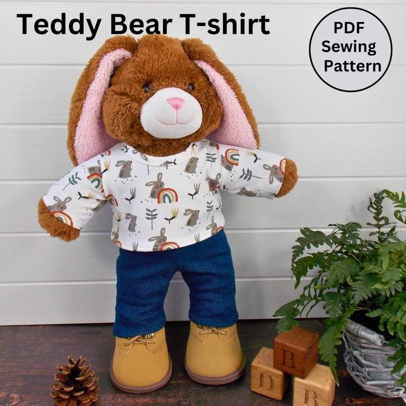Brown Build a Bear teddy wearing a white patterned t-shirt, blue trousers and sand coloured boots.  The text on the image reads 'Teddy Bear T-shirt' refers to the fact that this Etsy listing is for a sewing pattern to make a teddy bear t-shir.