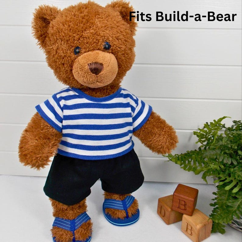 Brown Build a Bear teddy wearing a blue & white striped t-shirt and black shorts.  The text on the image reads 'Fits Build-a-Bear' refers to the fact that the t-shirt the teddy is wearing is made with a sewing pattern from Best Dressed Bears