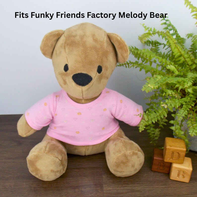 Brown Funky Friends Factory Melody teddy bear wearing a pink patterned t-shirt. The text on the image reads 'Fits Funky Friends Factory Melody Bear' refers to the fact that the t-shirt the teddy is wearing is made with a sewing pattern from Best Dressed Bears