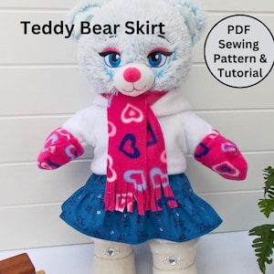 May include: A blue teddy bear wearing a white sweater, pink scarf with a heart pattern, and a blue skirt with white hearts. The bear is wearing white boots with rhinestones. The image includes the text "Teddy Bear Skirt" and "PDF Sewing Pattern & Tutorial".