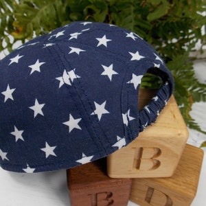 Pu&ograve; includere: Un berretto da baseball blu navy con stelle bianche stampate. Il berretto &egrave; appoggiato su tre blocchi di legno che compongono la parola "B-I-D".