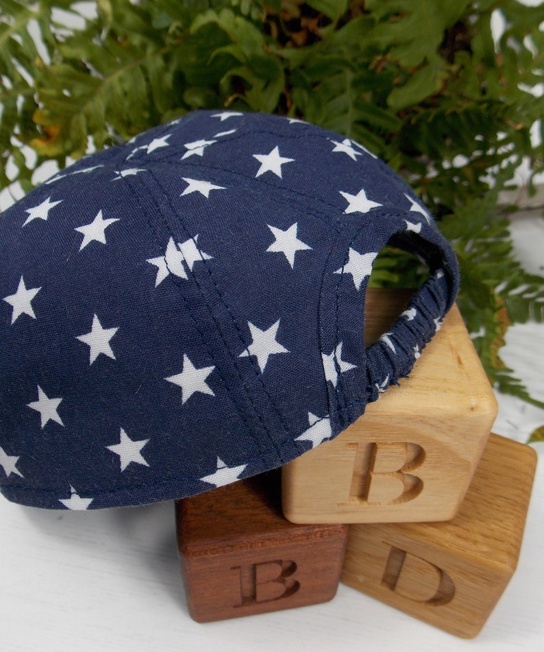 Pu&ograve; includere: Un berretto da baseball blu navy con stelle bianche stampate. Il berretto &egrave; appoggiato su tre blocchi di legno che compongono la parola "B-I-D".