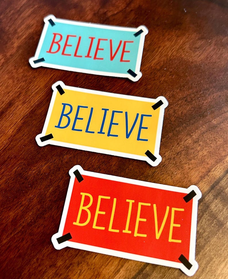 以下が含まれることがあります： 太字の「BELIEVE」という言葉が入った長方形のステッカー3枚。ステッカーの色は、赤字のライトブルー、青字のイエロー、黄字のレッドと様々です。各ステッカーには黒いコーナーアクセントが付いています。