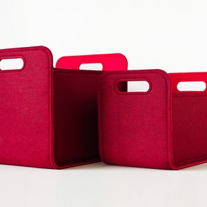 May include: Three red felt storage bins of varying sizes. Each bin has a rectangular shape with rounded corners and a handle cutout. The handles are a brighter red. The bins are designed for organizing and storage.