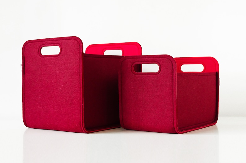 May include: Three red felt storage bins of varying sizes. Each bin has a rectangular shape with rounded corners and a handle cutout. The handles are a brighter red. The bins are designed for organizing and storage.