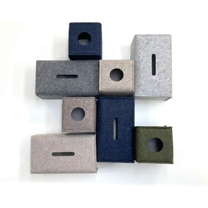 May include: An assortment of felt tissue box covers in various colors, including navy blue, gray, and olive green. The covers have either a circular or rectangular opening for tissue dispensing. The arrangement is against a white background.
