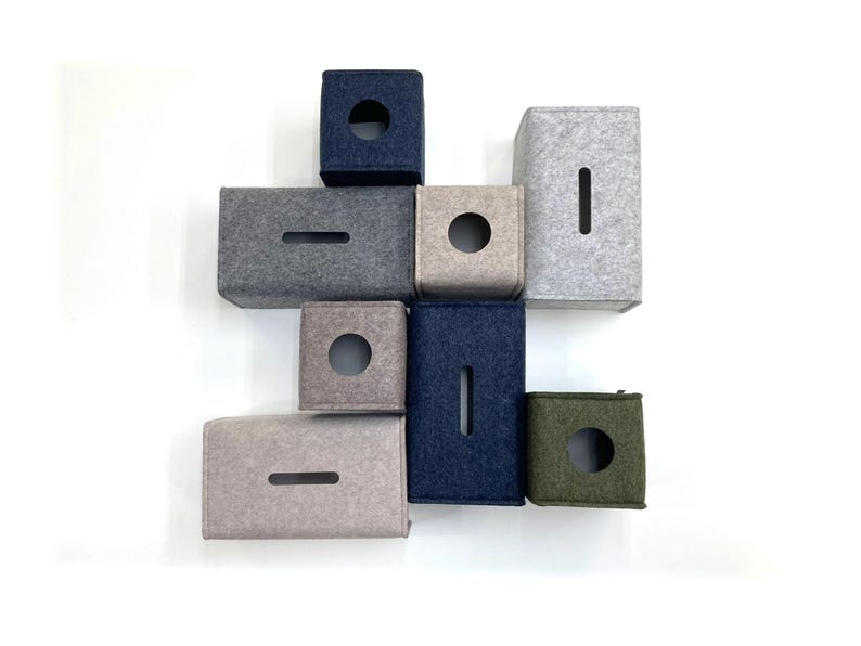 May include: An assortment of felt tissue box covers in various colors, including navy blue, gray, and olive green. The covers have either a circular or rectangular opening for tissue dispensing. The arrangement is against a white background.