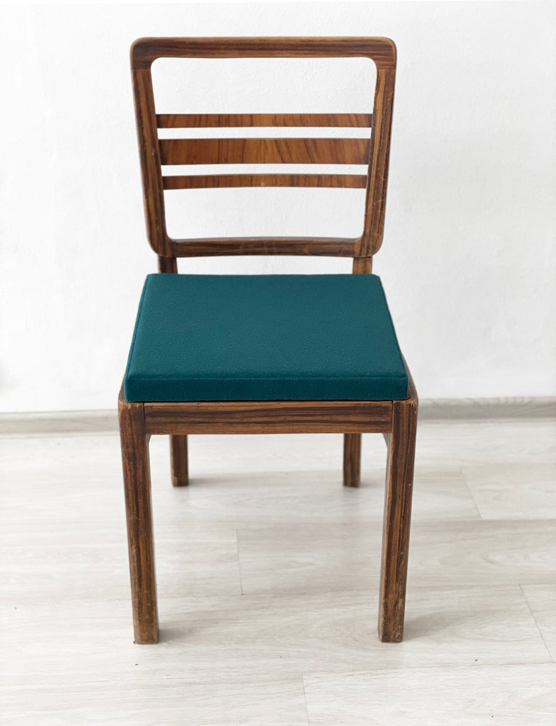 May include: A wooden chair with a dark green cushion. The chair has a simple design with a rectangular back and four legs.