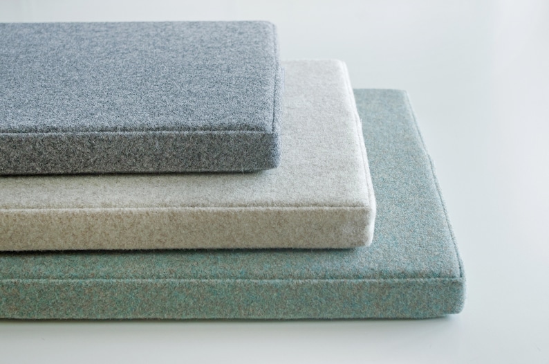 May include: Three rectangular cushions stacked on top of each other. The top cushion is gray, the middle cushion is beige, and the bottom cushion is light blue.