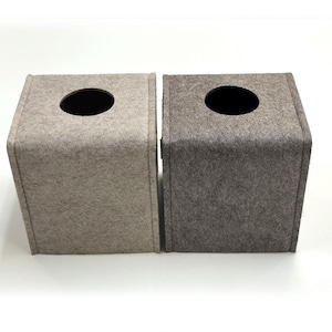 May include: Two square tissue box covers made of felt. One is light beige, the other is gray. Each has a circular opening on top for tissue dispensing. The boxes are side-by-side against a white background.