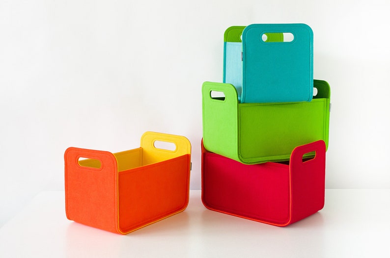 May include: A stack of colorful felt storage bins in red, green, teal, and orange. Each bin has a rectangular shape with a handle cutout. The bins are nested, showcasing their varying sizes and vibrant hues, perfect for organizing.