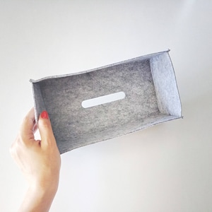 May include: A rectangular gray felt storage box with a white oval-shaped handle cut-out. The box is held against a white background. The felt material has a textured appearance.