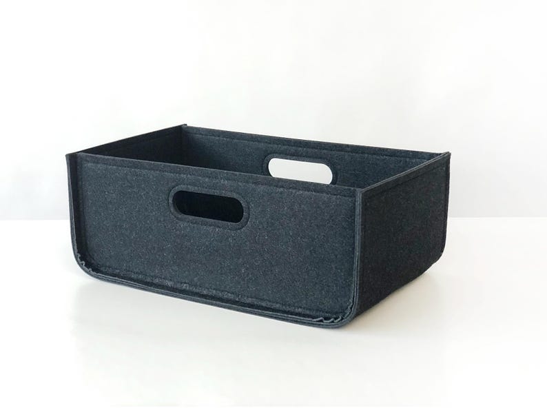 May include: A rectangular, dark gray felt storage bin with two handle cutouts. The bin is designed with a simple, modern aesthetic, suitable for organizing various items. The felt material provides a soft, textured appearance.