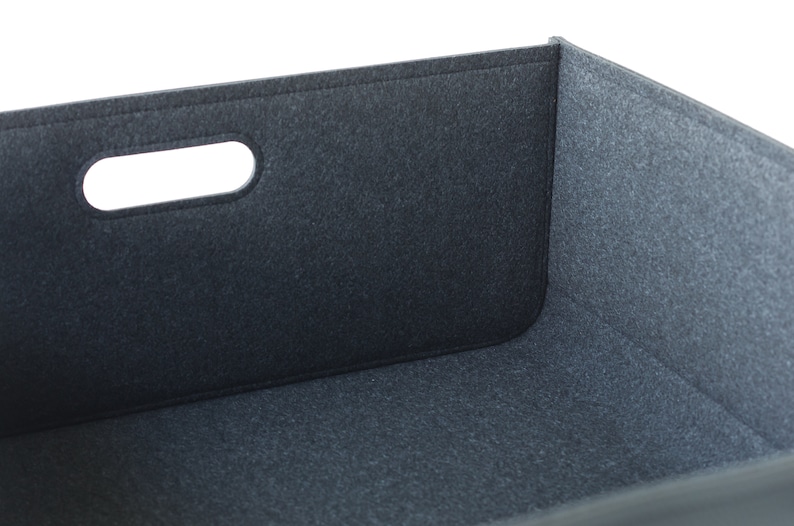 May include: A dark gray felt storage bin with a rectangular shape and a cutout handle. The bin has a simple, modern design and is made of a soft, textured material. The edges are neatly stitched.